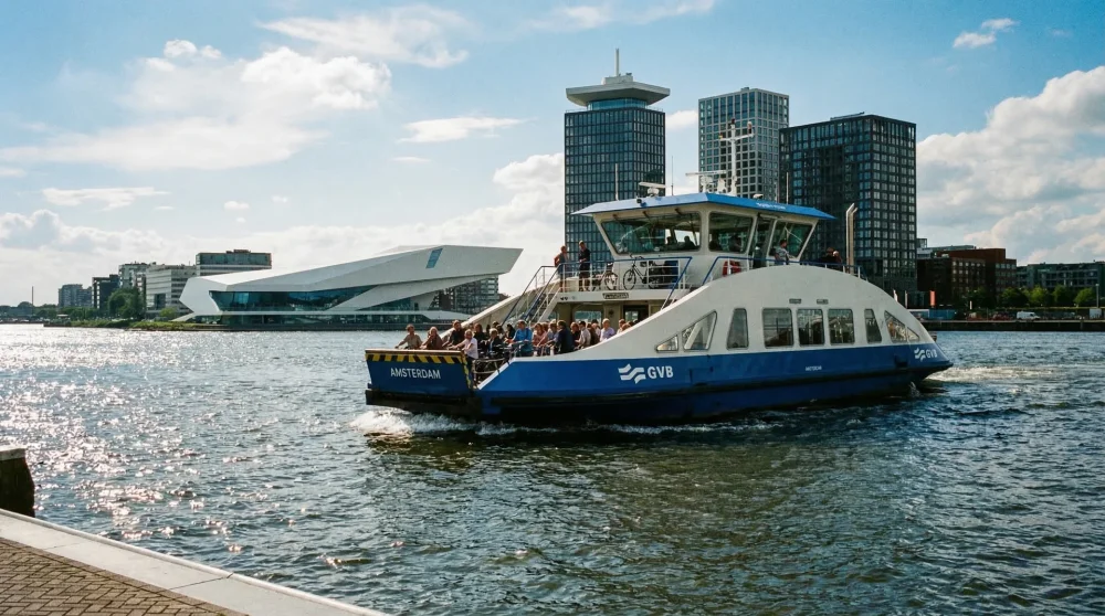 A blue and white GVB ferry transporting passengers across the River IJ with the modern Amsterdam Noord architecture in the background.