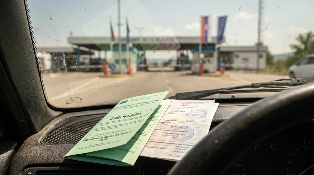 Physical Green Card insurance document and car registration papers placed on a car dashboard