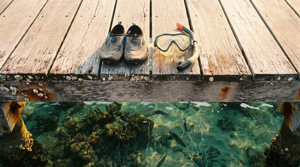 Wasserschuhe und Schnorchelmaske auf einem Holzsteg über klarem Wasser der Kaiman-Inseln