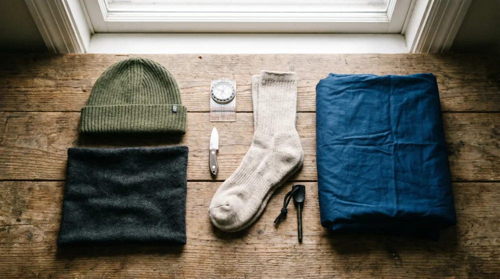 Winter camping accessories including merino wool beanie, neck gaiter, and thermal liner laid out on a tent floor