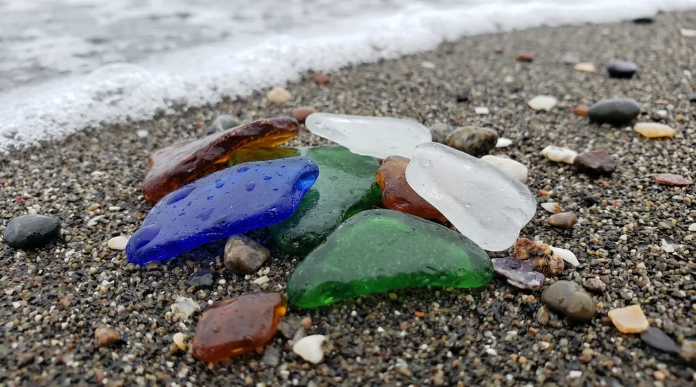 A collection of colorful sea glass pieces in blue, green, amber and clear arranged on wet sand at Glass Beach California