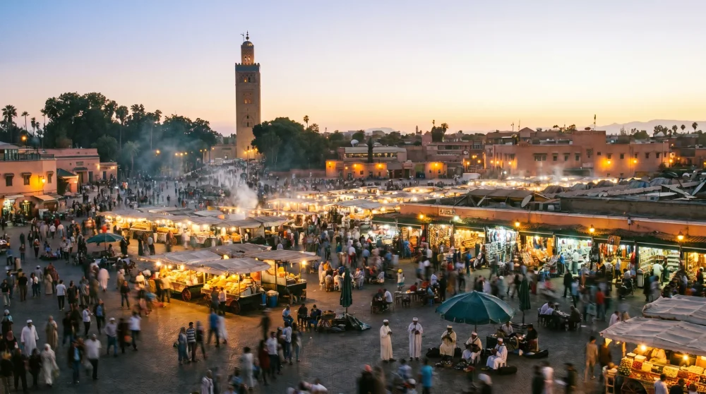 Bustling Jemaa el-Fnaa square in Marrakech at sunset with traditional market stalls and Koutoubia Mosque silhouette