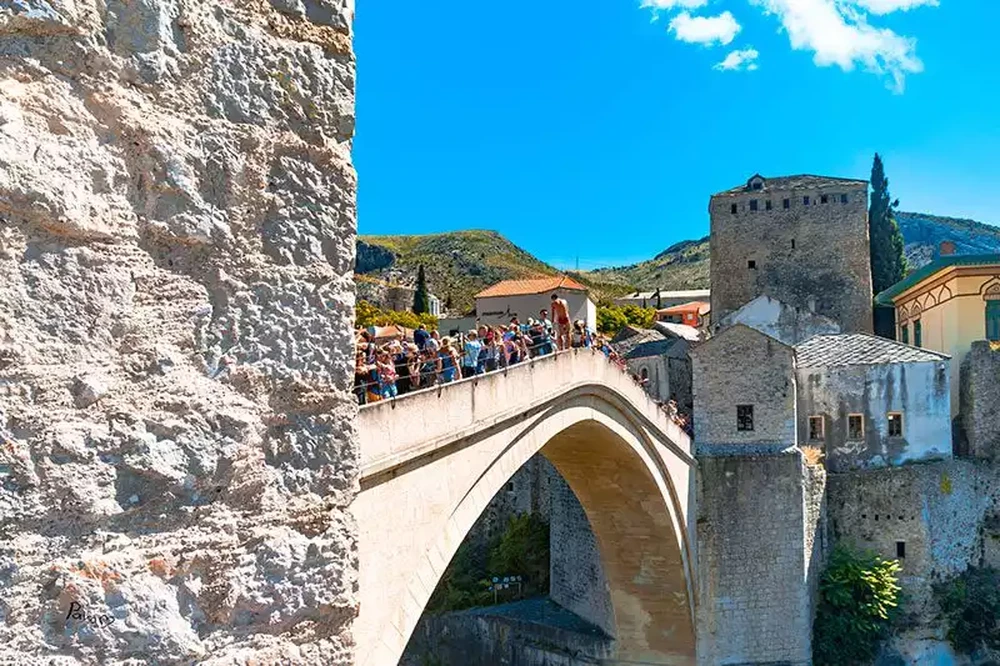 Close-up of Stari Most limestone arch with tourists walking across and a stone tower in the background