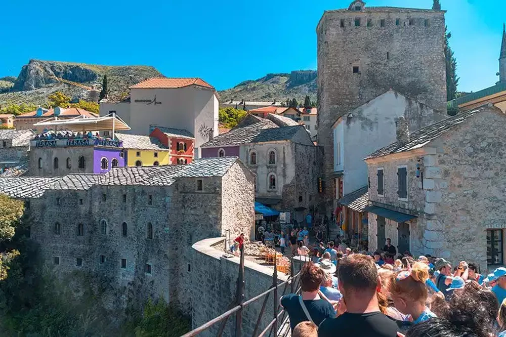 Crowded walkway in Mostar old bazaar near the bridge with stone buildings and terasa restaurant signs