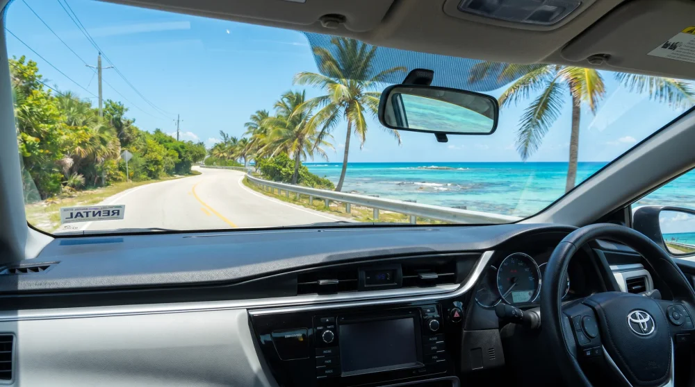Ein weißer Mietwagen fährt auf einer malerischen Küstenstraße im Linksverkehr auf Grand Cayman.