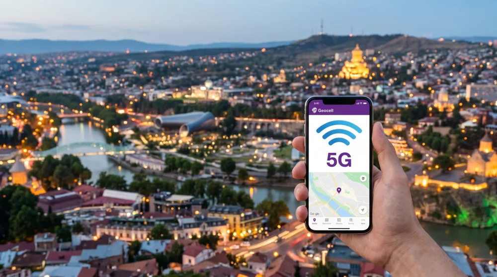 A person holding a mobile phone showing a strong network signal with the historic Tbilisi city center and Narikala Fortress in the background