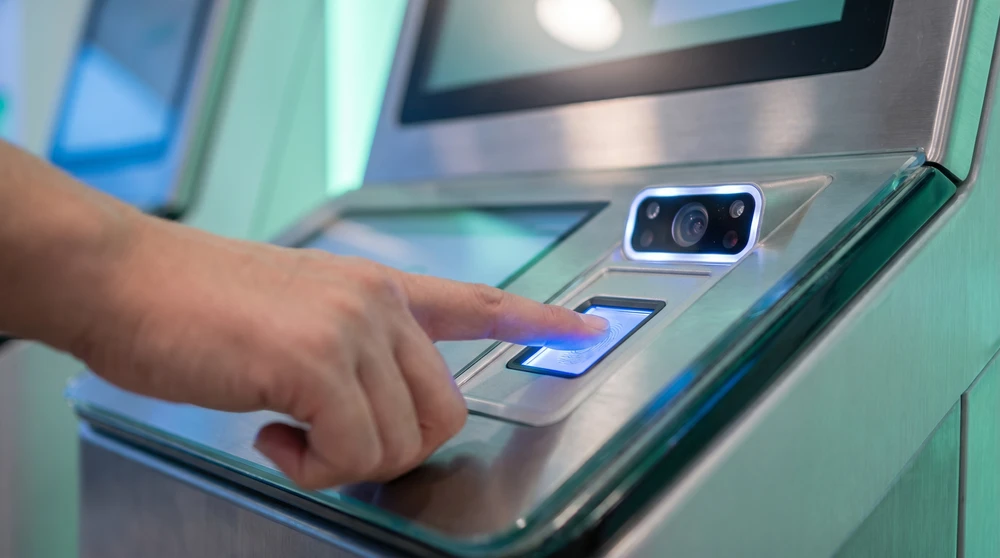 Hand auf einem beleuchteten biometrischen Kiosk mit Fingerabdruckscanner und Gesichtserkennungskamera an einer Grenze