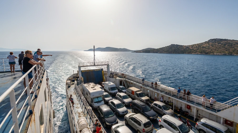 Car ferry crossing the blue Mediterranean channel with vehicles on deck and passengers at the rail