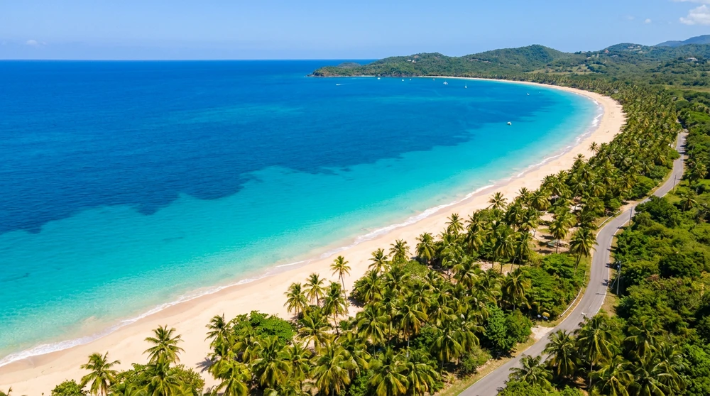 Aerial view of a curved Caribbean bay with turquoise water and a pale gold sand crescent.