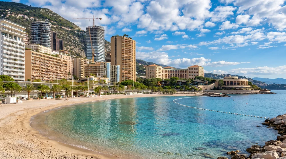 Sandy Larvotto Beach Monaco with turquoise water, city skyline and swimming area buoy line