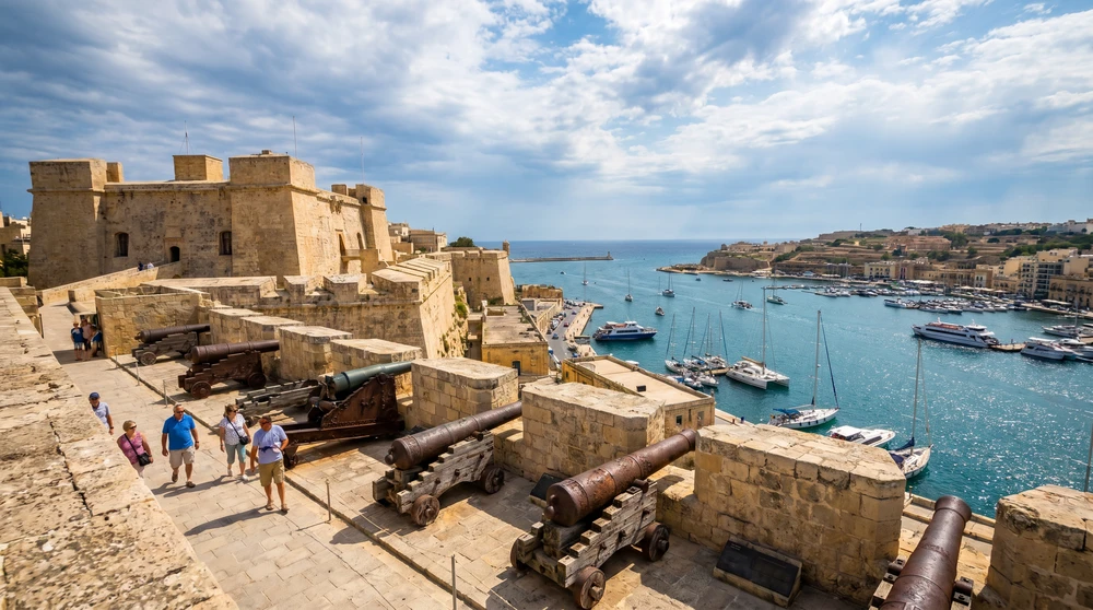 Sunlit limestone fortress ramparts with old artillery overlooking the harbour under a dramatic sky
