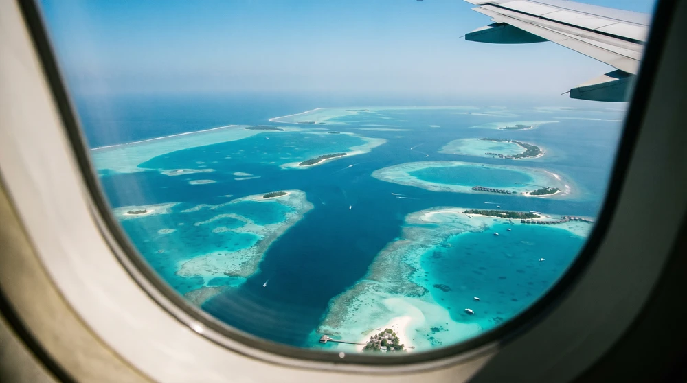 Blick aus dem Flugzeugfenster auf türkisfarbene Atolle und ringförmige Riffe der Malediven