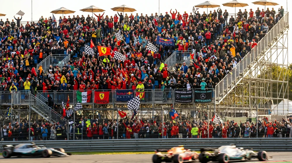 Packed grandstand crowd at Monaco Grand Prix with spectators and racing team flags