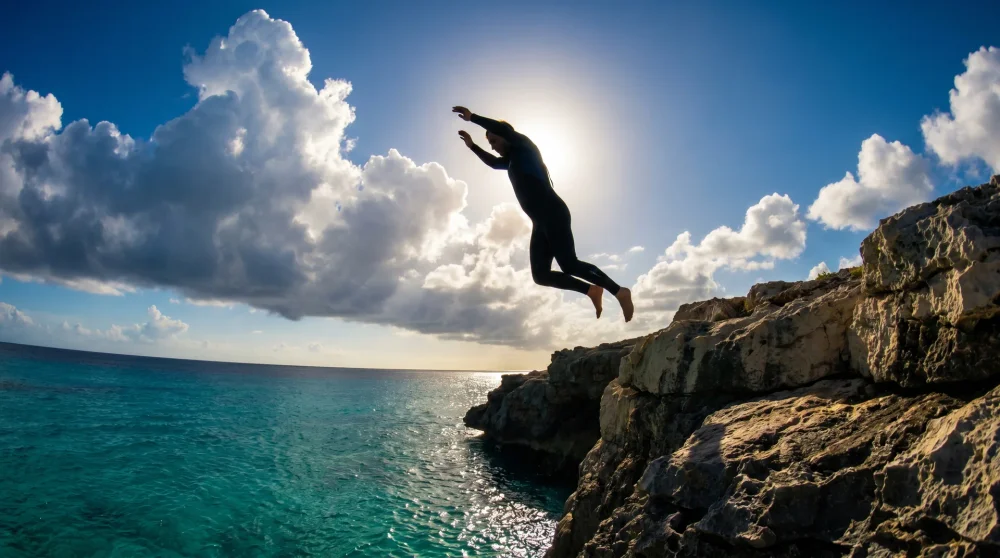 Person jumping feet-first from a limestone cliff into the turquoise Caribbean Sea at Negril Jamaica