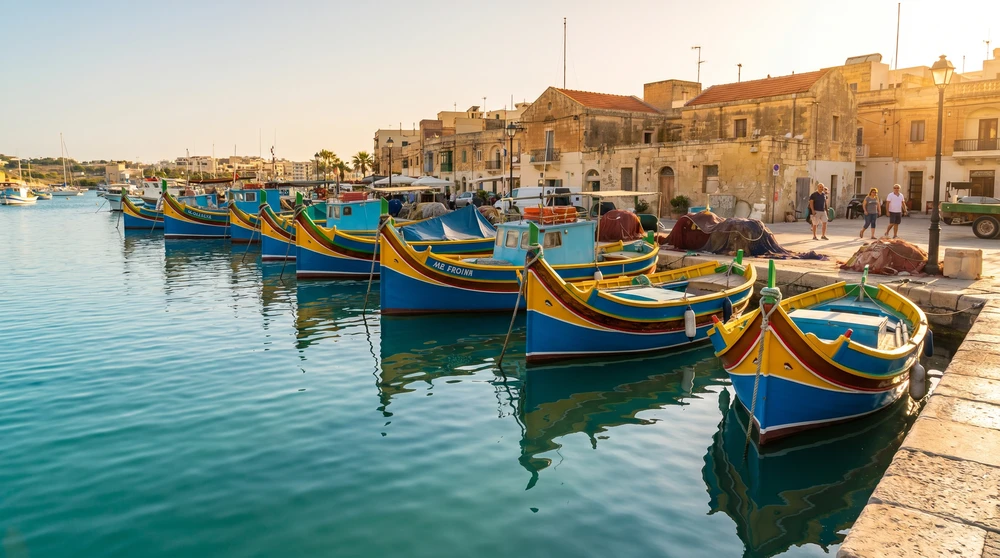 Brightly painted traditional Maltese luzzu fishing boats moored in a calm Mediterranean harbor at golden hour