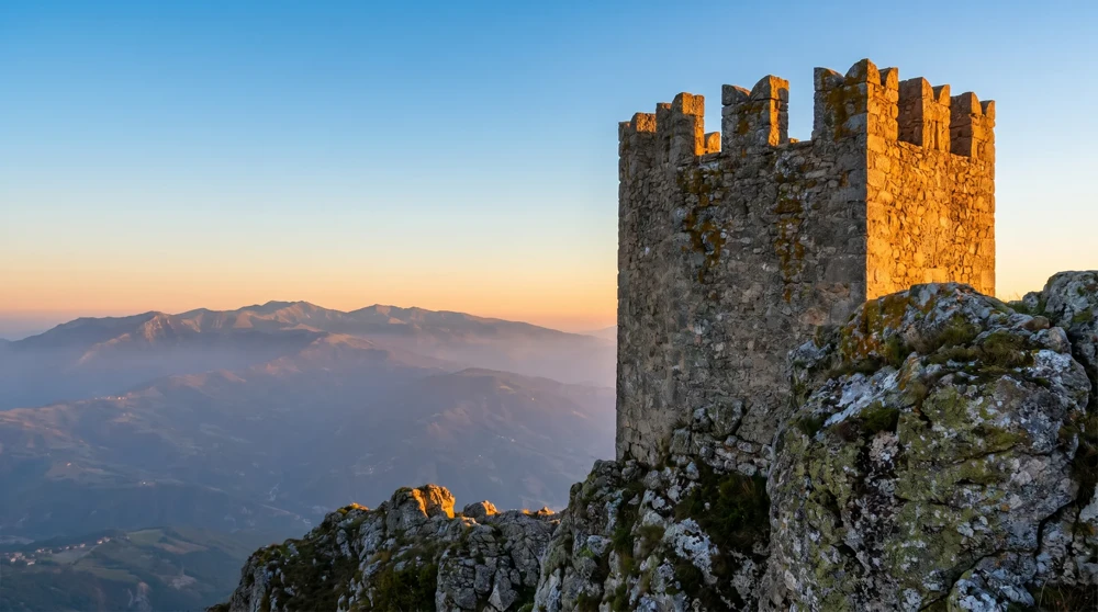 Medieval battlements of Torre Guaita, the First Tower of San Marino, silhouetted against sunrise with Apennine mountains in the background