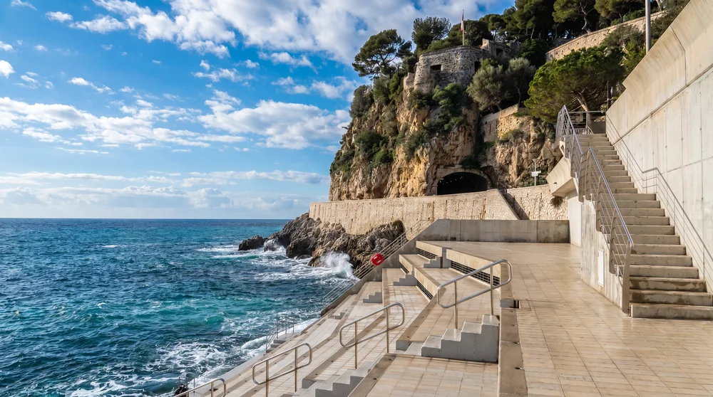 Terraced marble promenade at Solarium Beach Monaco with rocky cliff face tunnel and sea access steps