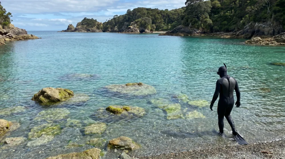 Schnorchler steigt ins klare felsige Wasser einer Kiesbucht auf einer griechischen Insel