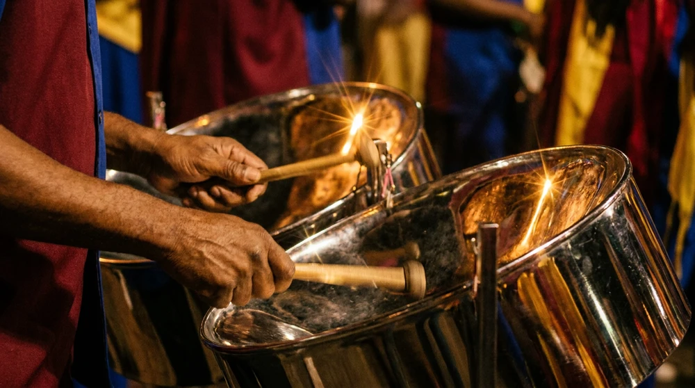Close-up of a steel pan drummer's hands striking tuned chrome pans under warm stage light.