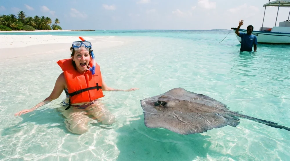 Beginner snorkeler with life vest at Stingray City Sandbar Grand Cayman, southern stingray passing below