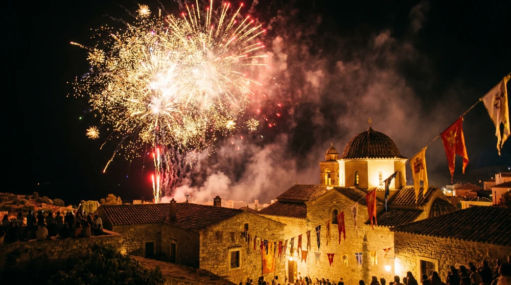 Buntes Feuerwerk bricht über einer traditionellen mediterranen Dorfskyline während eines sommerlichen Schutzpatron-Festas auf