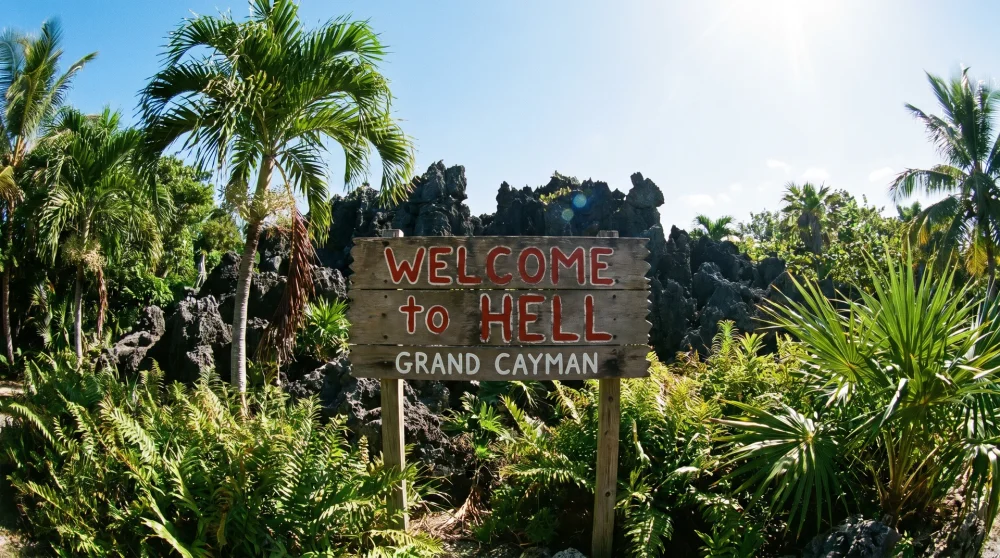 Das ikonische Welcome-to-Hell-Holzschild in Grand Cayman mit schwarzen Kalksteinfelsen im Hintergrund.
