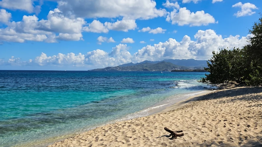 Magazine Beach Grenada white sand and vivid turquoise water with distant mountains under blue sky