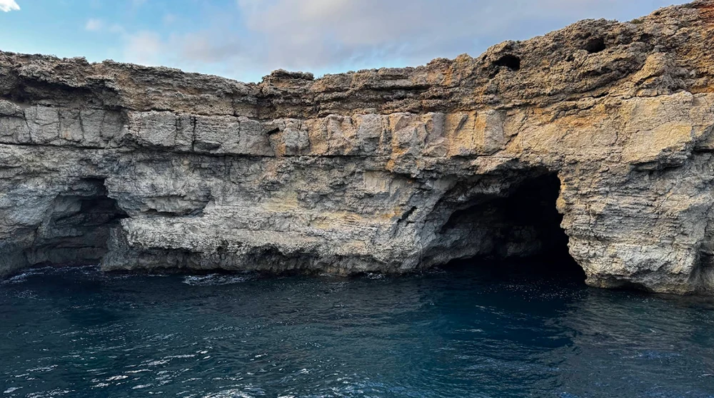 Eine große Meereshöhlenöffnung in den Kalksteinklippen nahe der Santa Marija Bucht auf Comino, mit tiefblauem Wasser am Eingang