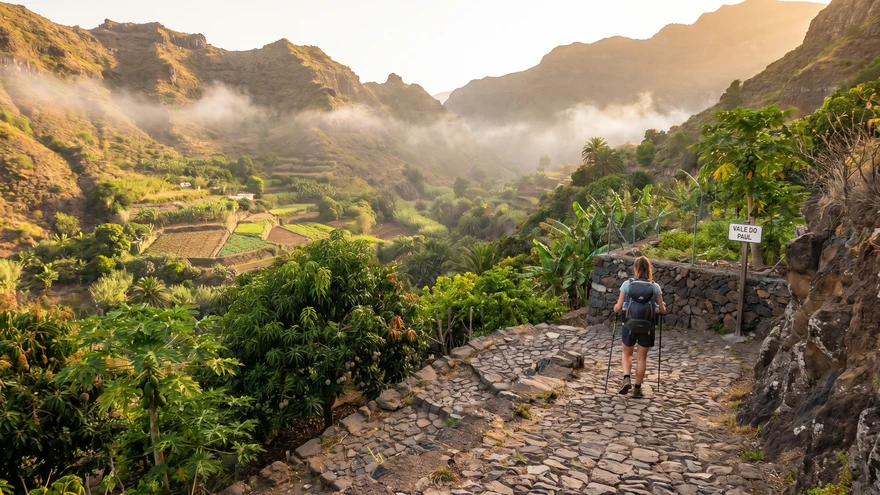 Hiker on steep cobblestone trail descending from Cova crater through morning mist into the green Paul Valley