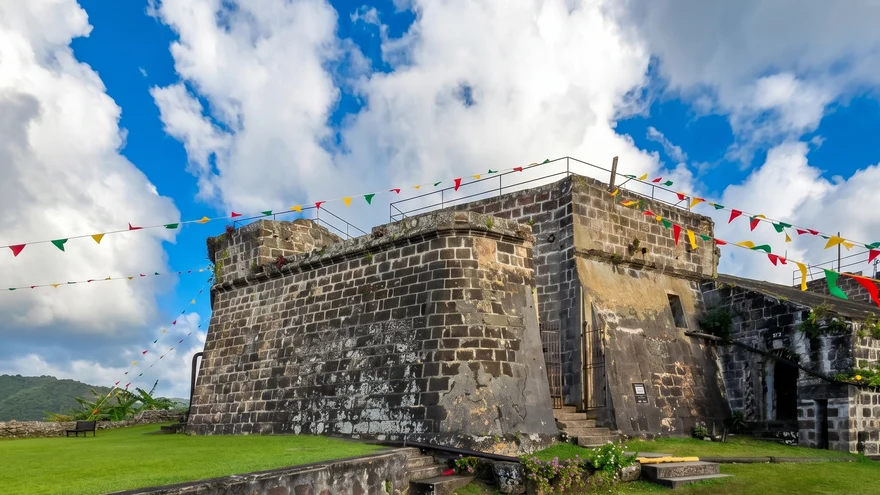 Fort Frederick Grenada stone battlements with colorful bunting flags against vivid blue sky and green hillside