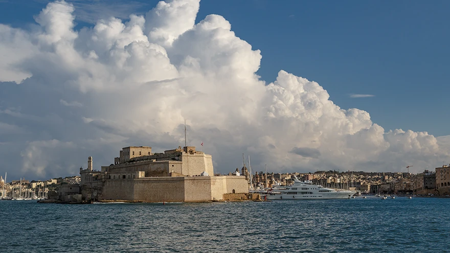 Fort St Angelo vom anderen Ufer des Grand Harbour aus gesehen, seine Kalksteinbastionen ragen unter dramatischen Wolken ins Wasser, Birgu, Malta