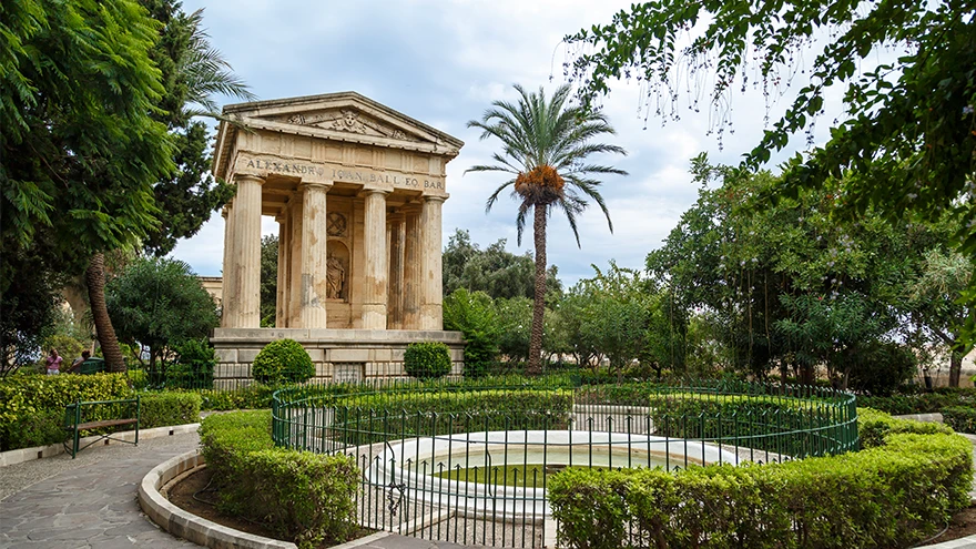 The neoclassical Sir Alexander Ball monument among formal hedges and a palm in the Lower Barrakka Gardens, Valletta