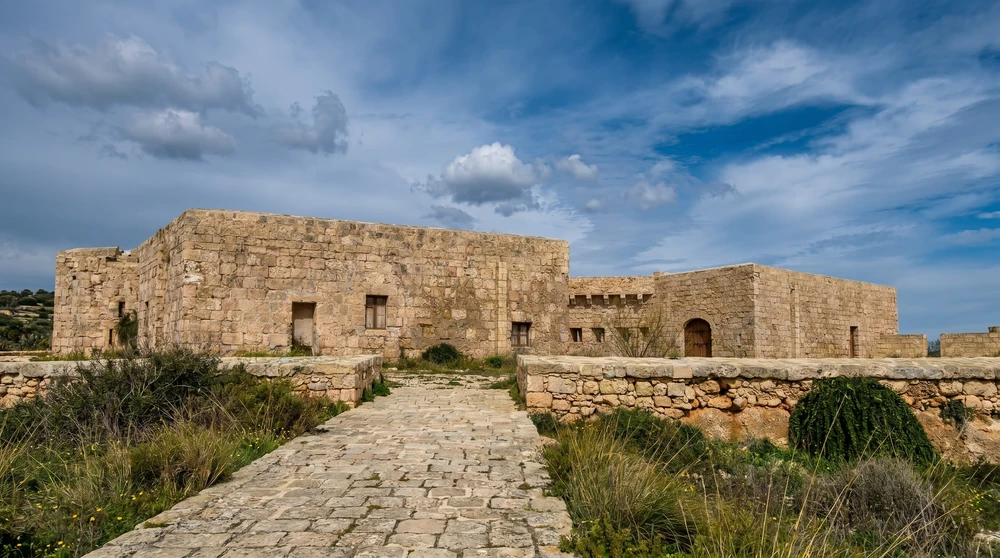 A long low stone coastal redoubt in Malta with thick walls and a paved approach under a cloudy sky