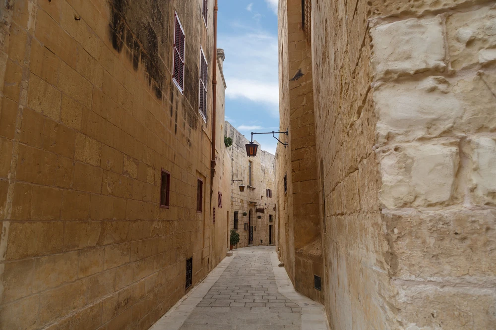 Narrow limestone alley between honey-coloured stone buildings in Mdina's silent old town, Malta