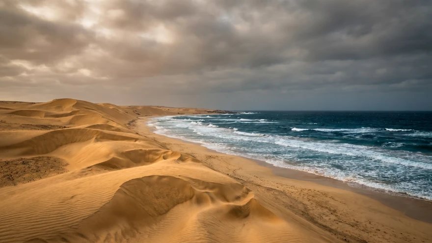 Towering wind-sculpted sand dunes meeting the Atlantic Ocean at Praia de Chaves in Boa Vista, Cabo Verde