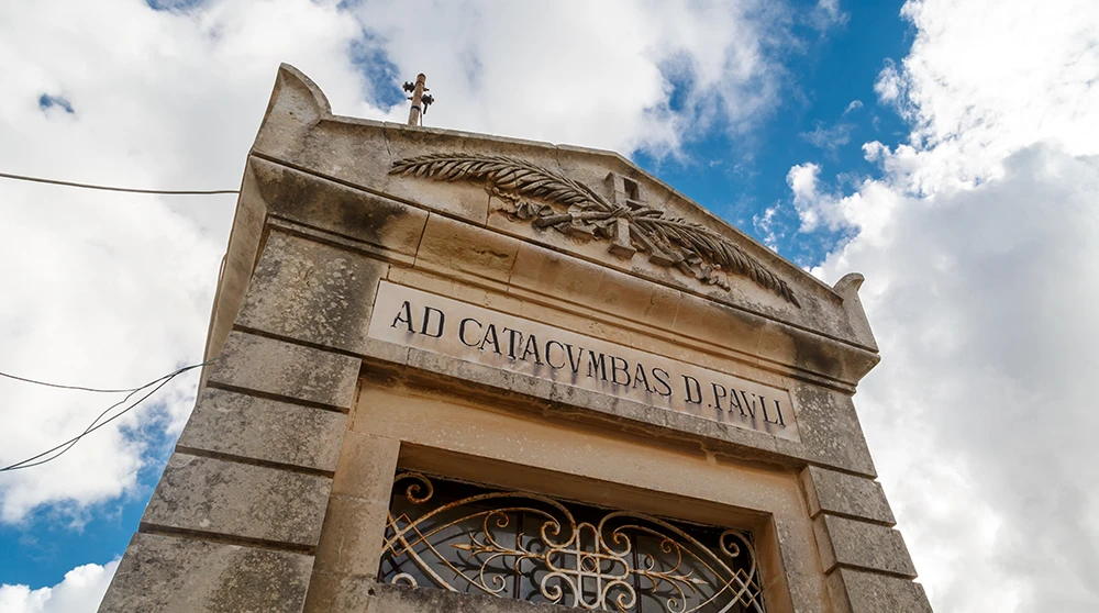 Das steinerne Eingangsbogenportal der St. Pauls Katakomben in Rabat mit der Inschrift AD CATACVMBAS D PAVLI unter bewölktem Himmel