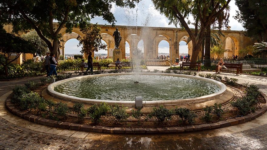 The central fountain and shaded stone arcade of the Upper Barrakka Gardens busy with visitors in Valletta
