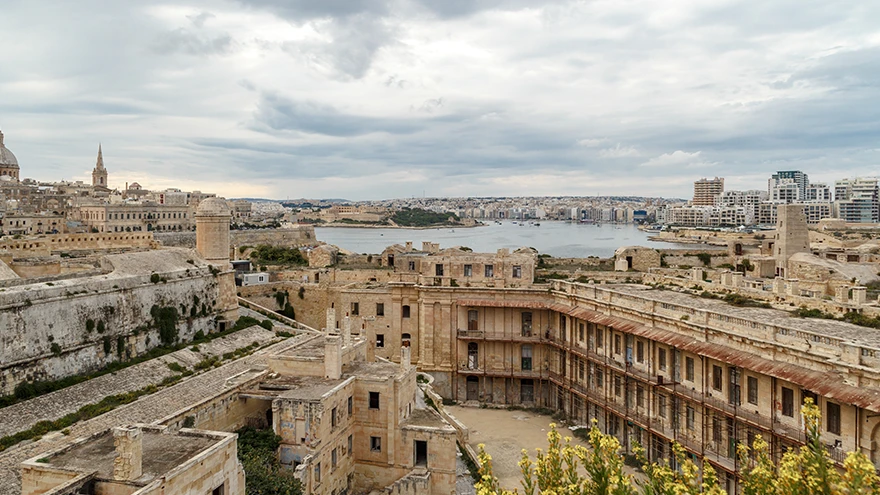Blick über den Marsamxett Harbour von Vallettas alten Befestigungsanlagen zur modernen Skyline von Sliema unter bewölktem Himmel