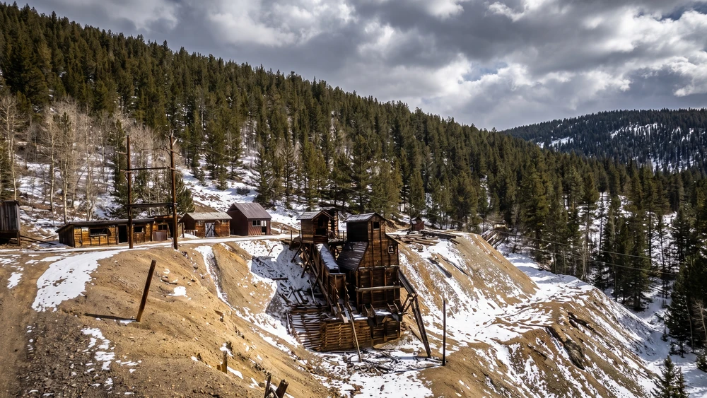 Snow-covered stamp mill and mining outbuildings in the ghost town of Bonanza, Colorado, backed by pine forest.