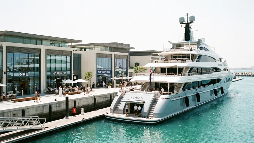 Superyacht docked at a modern marina with boutique shops along the waterfront