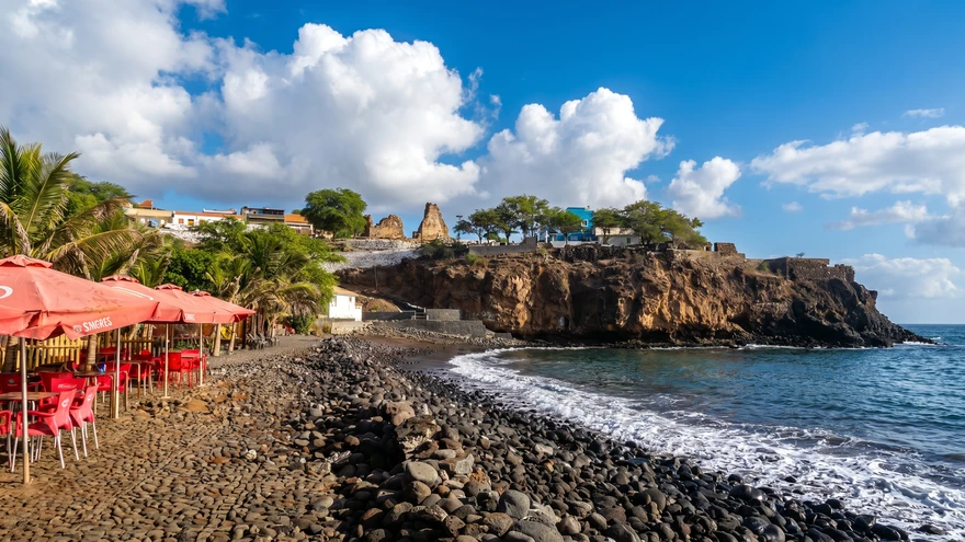 Rocky beach and seaside cafe along the Cidade Velha waterfront with ruins in the background