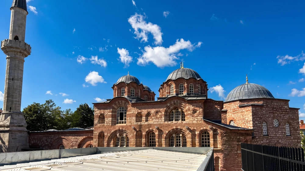 Fethiye Mosque exterior in Istanbul with Byzantine brickwork, domes, and a tall minaret under a blue sky.