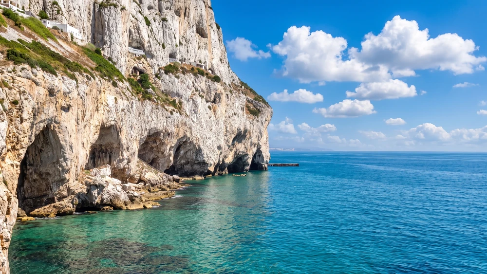 Steep limestone cliffs along Gibraltar's southeastern coast with cave openings visible just above the turquoise sea.