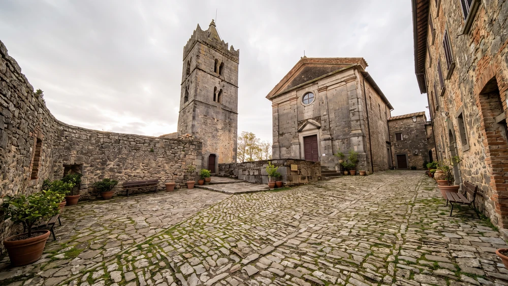 Stone bell tower and the Church of the Assumption inside Hum's medieval walls under an overcast Istrian sky.
