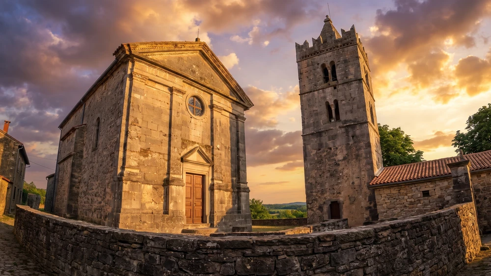 Church of the Assumption and its bell tower in Hum lit by golden sunset light against a dramatic sky.
