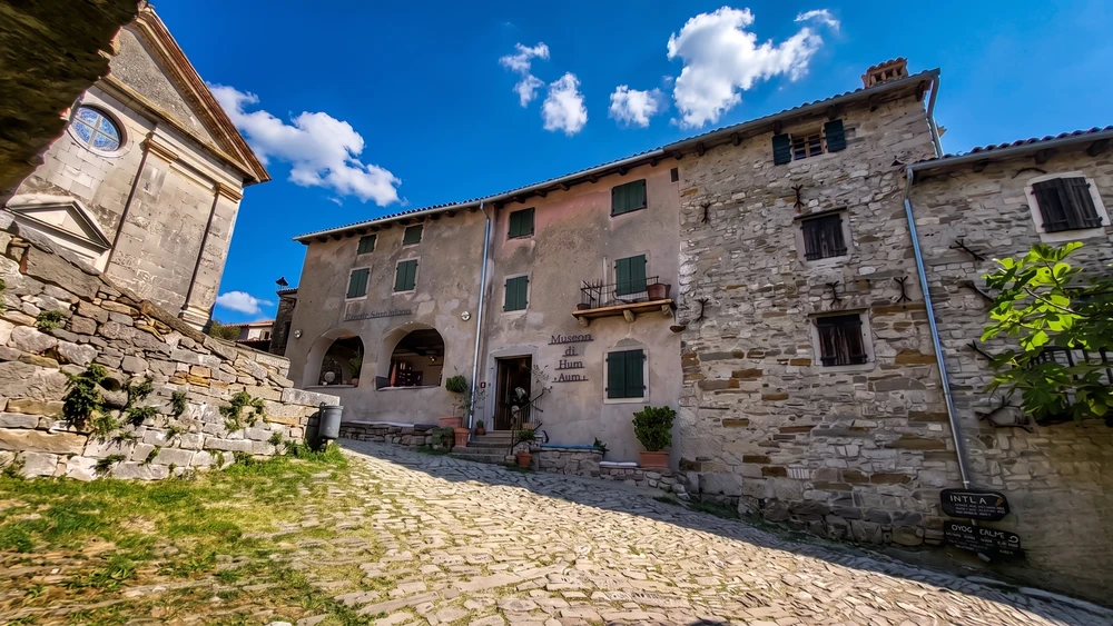Stone facade of the Museum of Hum with green shutters along a narrow cobblestone street inside the walls.