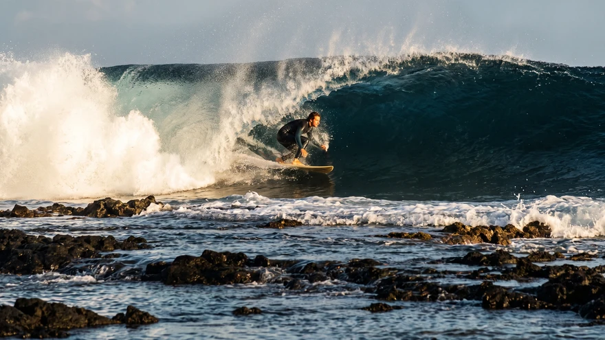 Surfer riding a hollow wave over the shallow volcanic reef at Ponta Preta, Sal