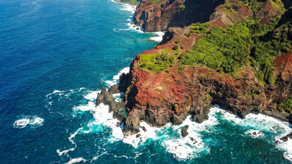Aerial view of a red-soil cliff and rugged coastline near Ship's Landing Point on Pitcairn Island