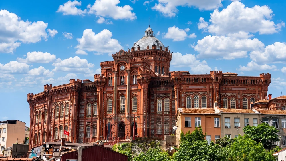 Church of St. Mary of the Mongols in Istanbul with a red Byzantine facade, domed tower, and blue sky.