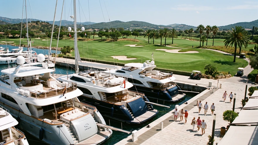 Luxury marina with mega-yachts docked beside a manicured golf course
